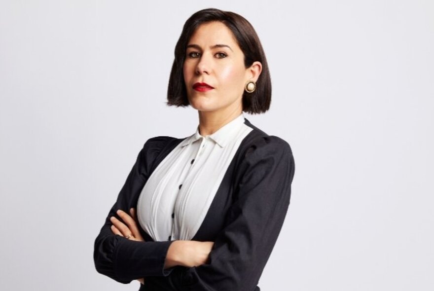Journalist Jan Fran with arms crossed looking serious in a buttoned up shirt and cardigan.