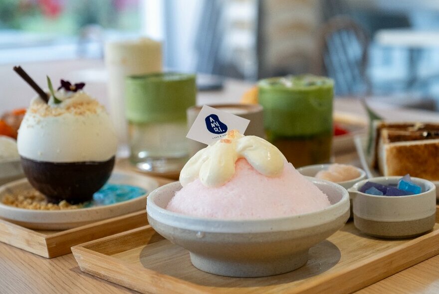 Asian-style desserts featuring a bowl with pink shaved ice and a creamy topping that looks like a flower. 