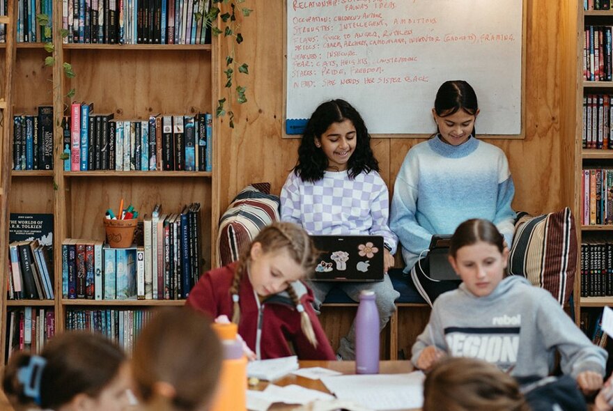 Young writers seated with paper and laptops in a room lined with books.