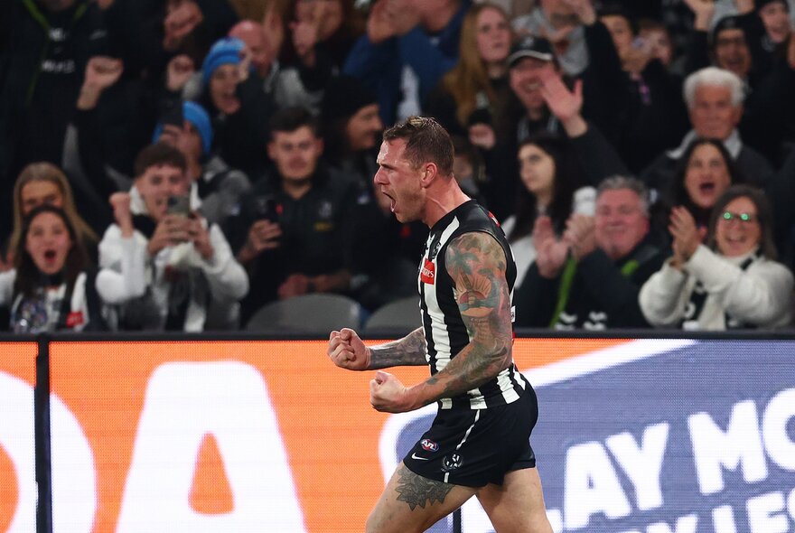 A Collingwood football player celebrates on field with fists clenched. 
