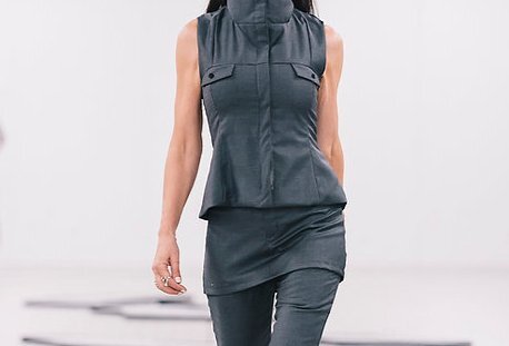 A model on the catwalk wearing a grey vest, pants and mini skirt.
