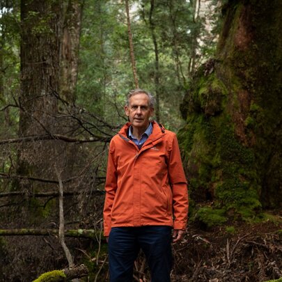 Dr Bob Brown standing wearing an orange jacket in a rainforest. 