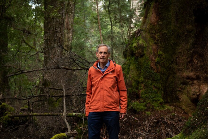 Dr Bob Brown standing wearing an orange jacket in a rainforest. 