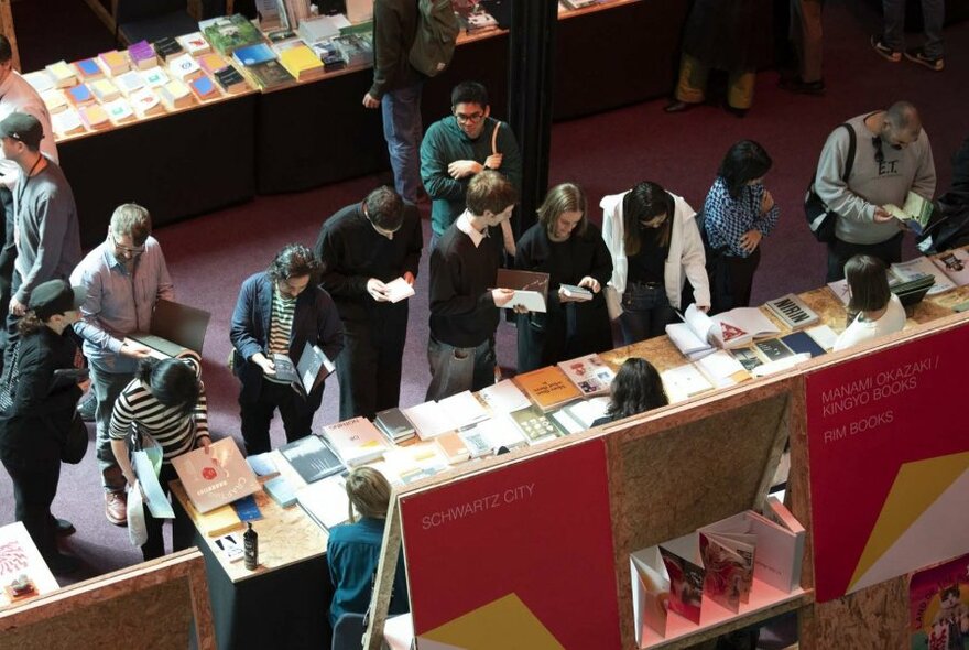 Overhead view of a crowd of people browsing books at book stalls in an interior setting.