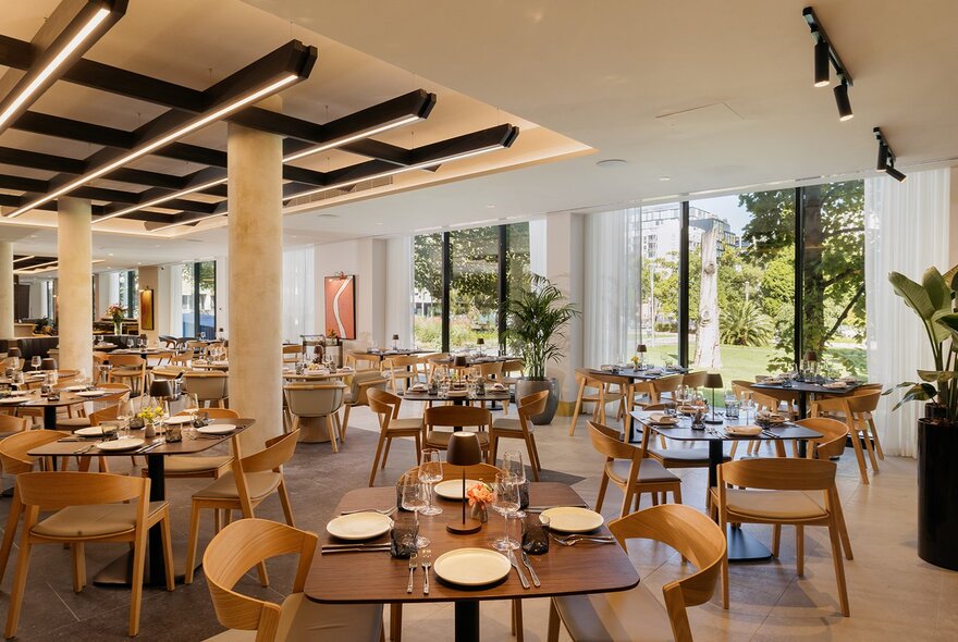 Modern restaurant dining room at Fico, with many tables and chairs arranged in the airy space, large glass windows lining one wall.