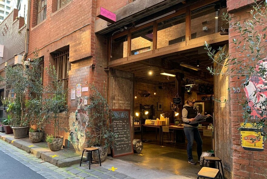 Large entranceway in tall red brick buying with olive trees in pots along the exterior wall.