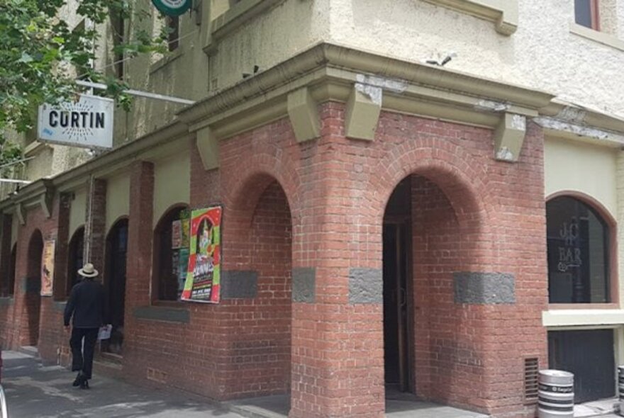 Man wearing a hat walking past the Curtin Hotel exterior with arched brick entry.