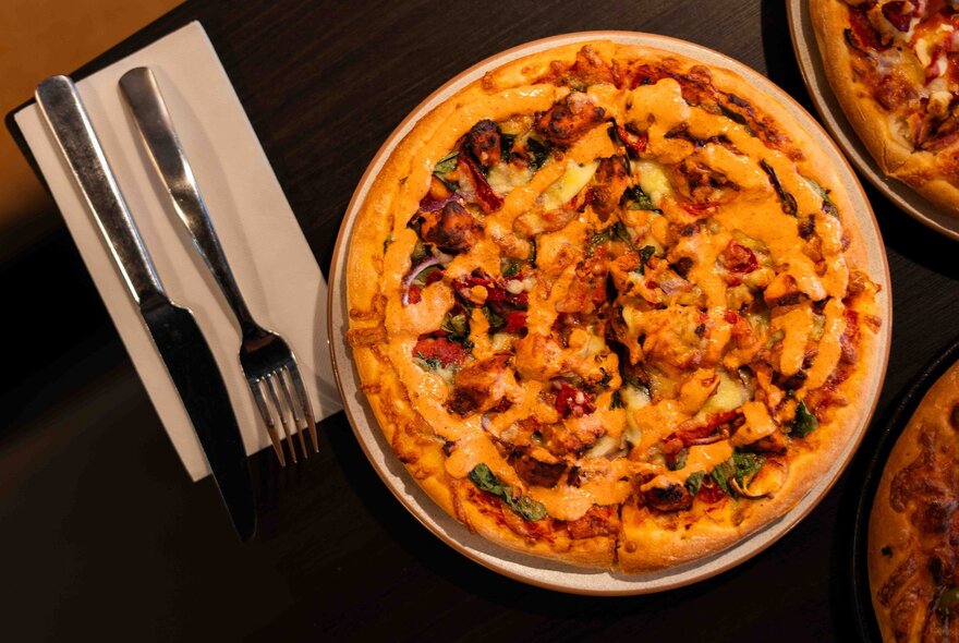 Looking directly down on a pizza on a plate with cutlery next to it. 