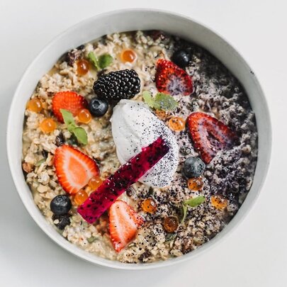 A bowl of fruit and grain porridge or muesli topped with berries, yogurt, and a vibrant garnish.
