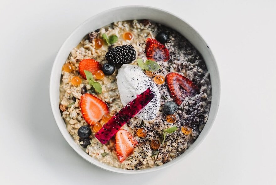 A bowl of fruit and grain porridge or muesli topped with berries, yogurt, and a vibrant garnish.