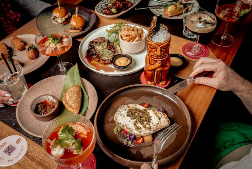 A table in a restaurant filled with plates of food and drinks with a pair of hands holding cutlery above a plate.