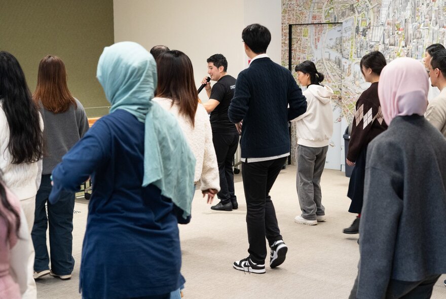 An interactive dance workshop in a studio, where participants are learning a dance following instructions from a man holding a microphone.