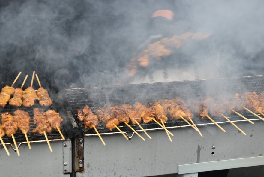 Skewers of meat being cooked on an open grill at a food stall.