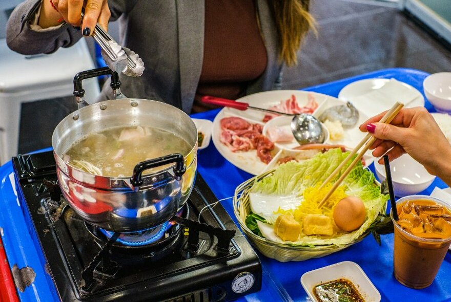 Diner cooking hotpot on a bright blue table.