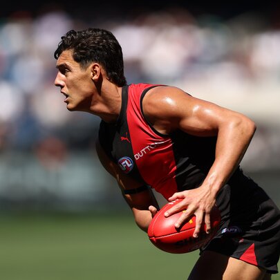 An Essendon AFL player holds the ball and crouches over slightly on the run. 