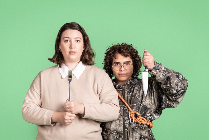 Two individuals posing in front of a solid green background, one holding a fork, the other holding a chef's knife. 