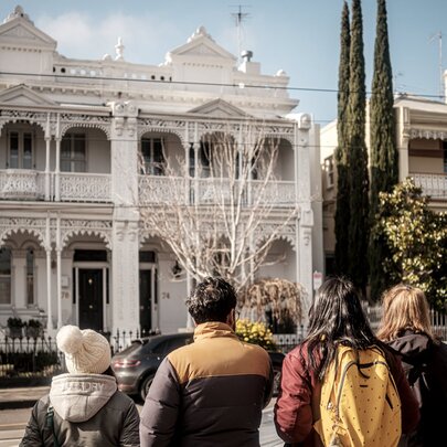 A group of people on a walking tour in a South Yarra street looking at two white terrace houses.