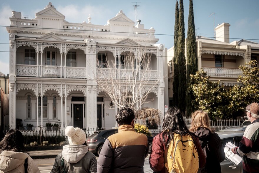 A group of people on a walking tour in a South Yarra street looking at two white terrace houses.