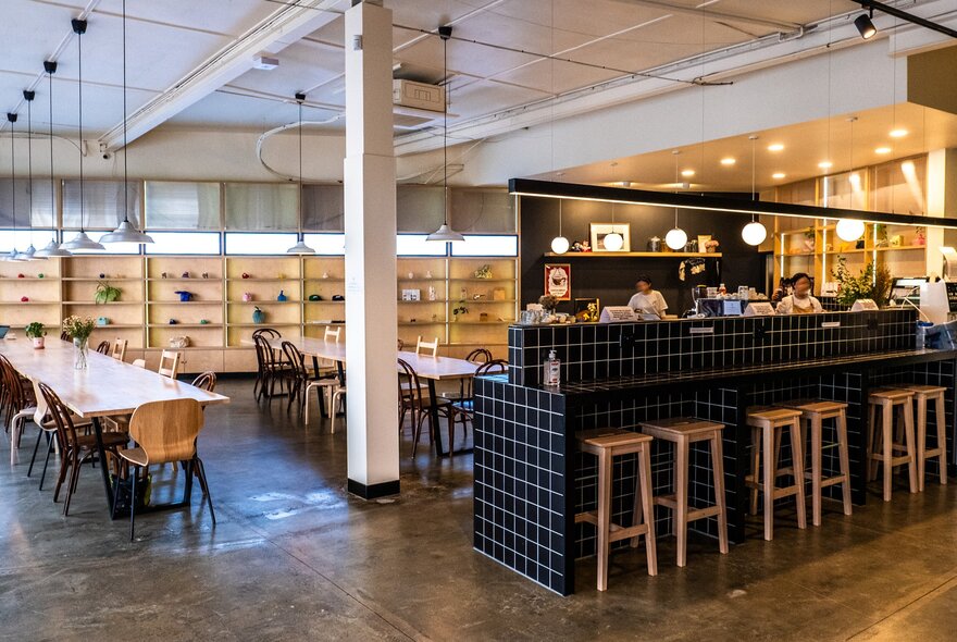 Inside a modern cafe. There are people making coffees at the counter and a shelf with ceramics at the back of the room.