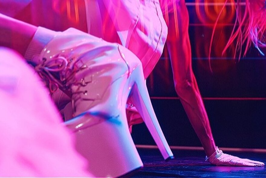 A white platform stiletto boot on a dancer bending backwards.
