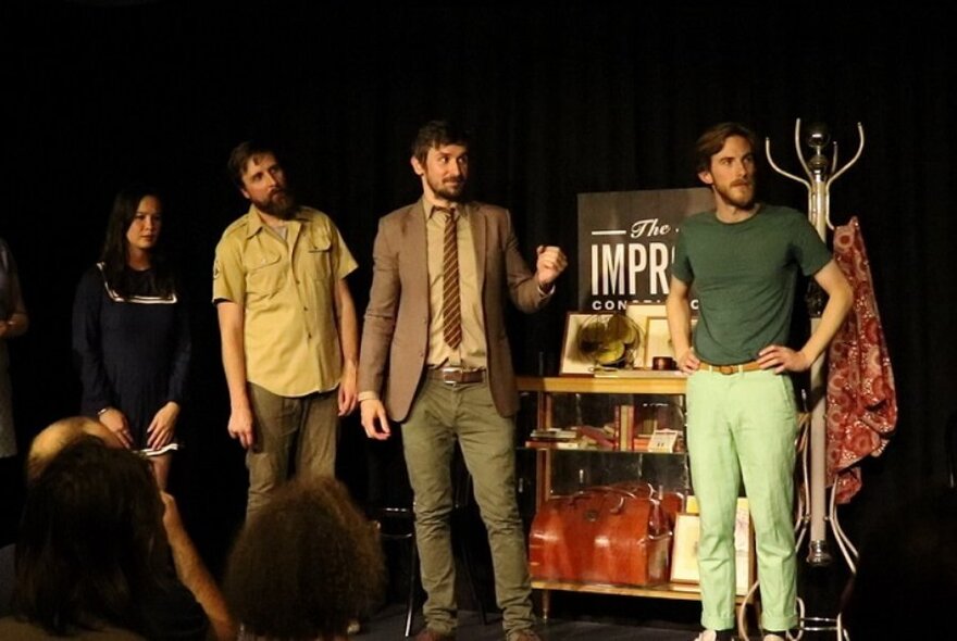 Four people on stage set, all looking to the left.