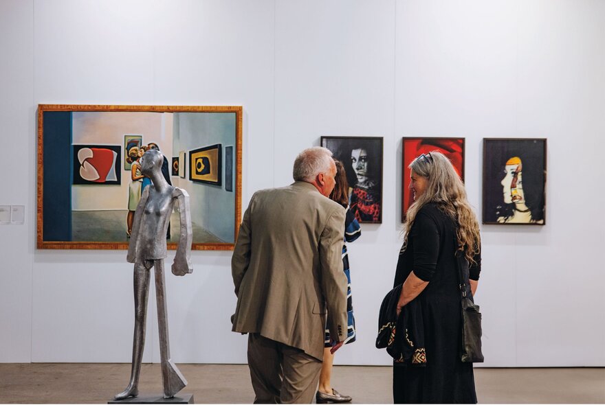 People looking at artworks on a gallery wall with metal sculpture.