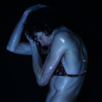 A dark image of a wet woman in a bikini top curling her body with her arms on clasping her head. 