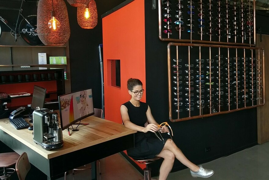 Person looking at a pair of glasses and many glasses on racks on the wall of an optician's