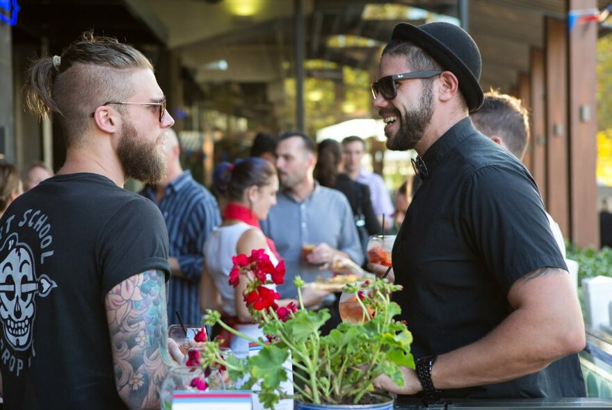 Patrons standing outside in the outdoor area of BearBrass drinking, smiling and conversing.