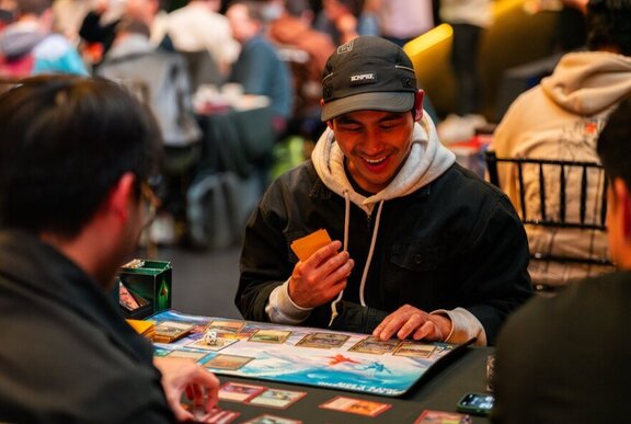 Two friends playing a board game at Fortress Melbourne, one of them smiling while holding cards in his hands.