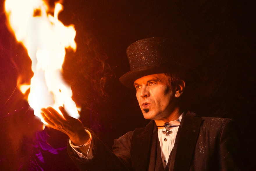 Magician wearing a top hat with flames issuing from his outstretched hand.