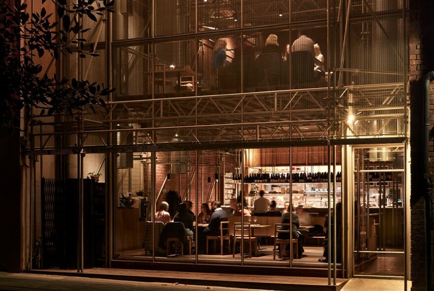 Street view of the glass walled exterior of Sunda restaurant showing diners seated at tables inside and a kitchen in background.