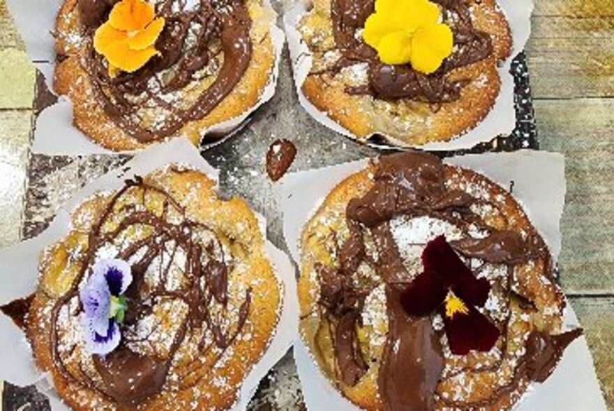 Four pasties topped with chocolate sauce and a pansy each. 