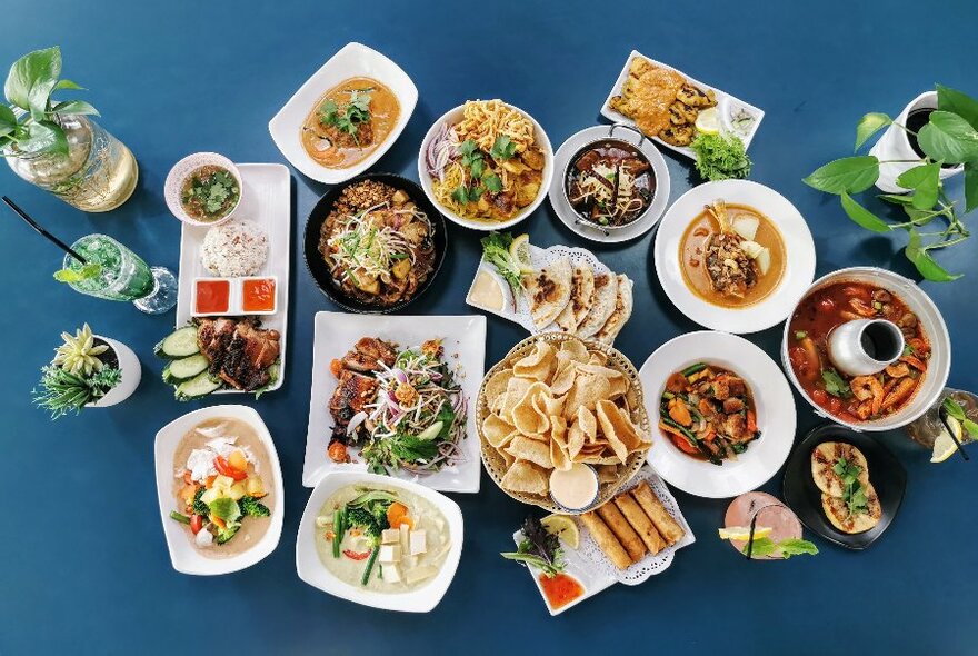 Looking down on a blue table laden with many plates and bowls of Thai food. 