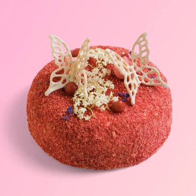 A small, round red cake decorated with white chocolate butterflies and small white and red edible embellishments.