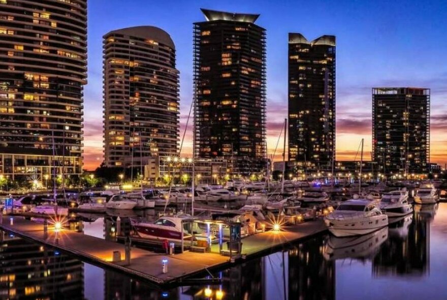 Docklands at sunset with lights of tall buildings reflected in the water.