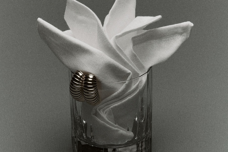 Sculptural fabric with metal earrings displayed on a glass vessel.