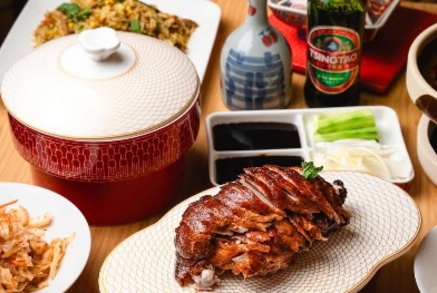 A selection of Chinese food, including a peking duck, displayed on traditional Chinese platters on a table.