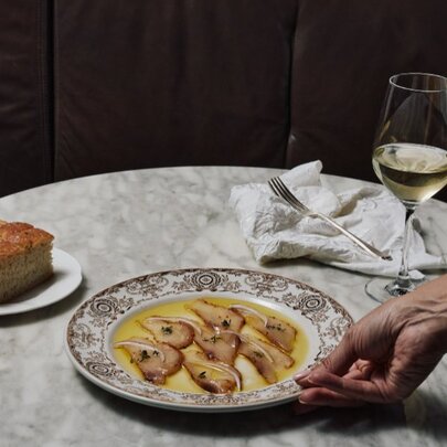 Hand positioning a plate of cod, cake and wine on a marble table.