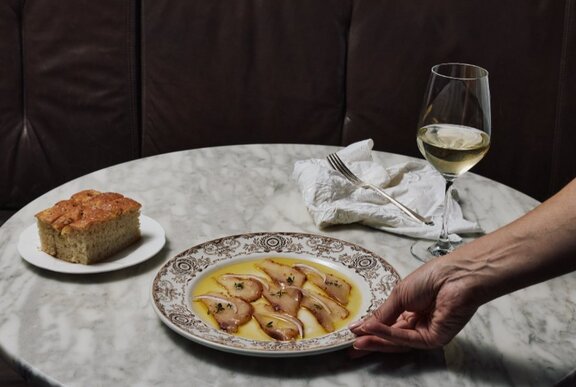 Hand positioning a plate of cod, cake and wine on a marble table.