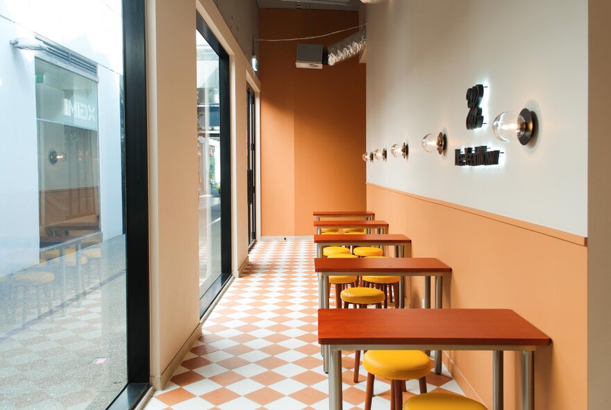 Cafe seating with small red tables and yellow stools on a peach and white chequered floor.