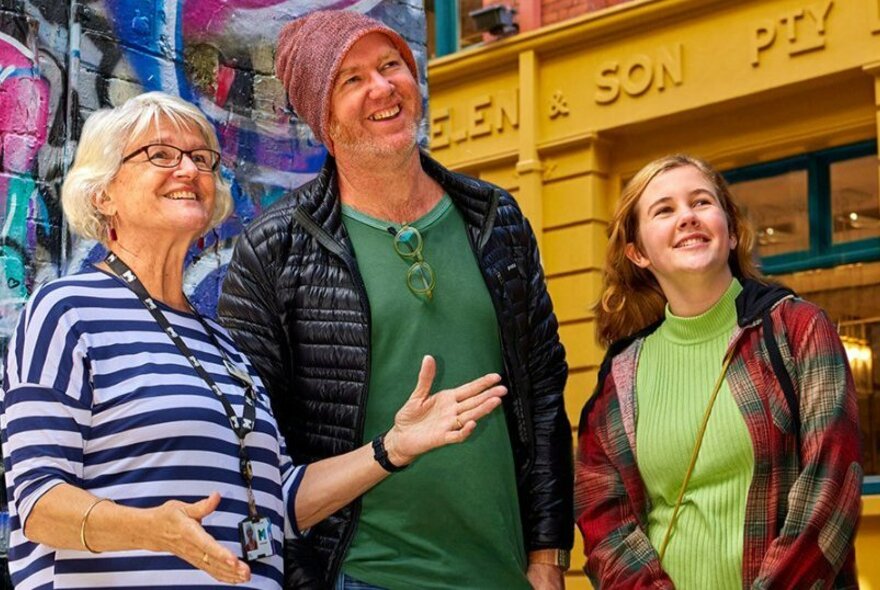 A young tourist couple and an older tour guide, standing in front of a famous Melbourne pub.