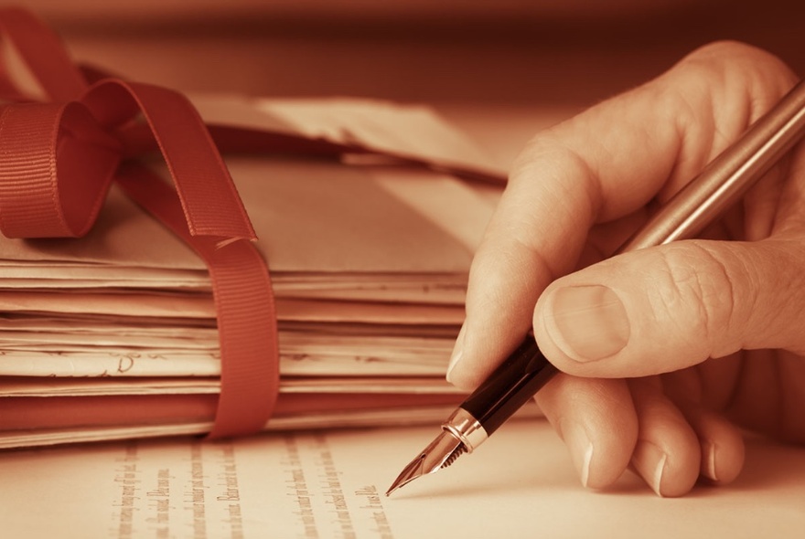 Close-up of a hand holding a fountain pen and writing on paper.