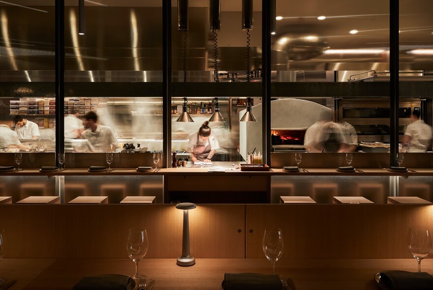 Looking through from a dining room into an active kitchen with chef's in blurred motion. 