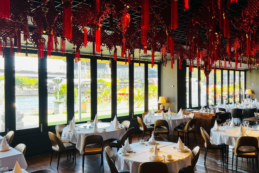 Restaurant interior decorated for Chinese New Year with red lanterns and ribbons, tables set for dinner overlooking Docklands waterway.