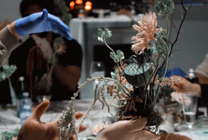 A person creating an Ikebana arrangement at a table with other people doing same. 