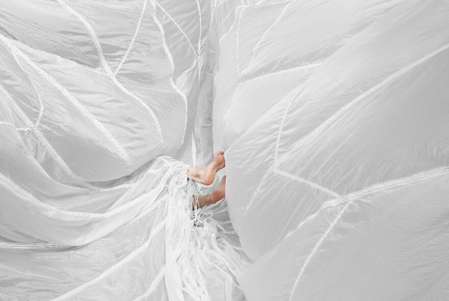 A pair of feet poking out from masses of white parachute silk.