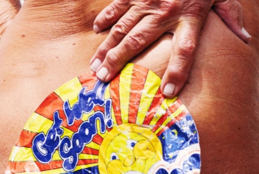 Person holding an old sticker to the base of their spine.