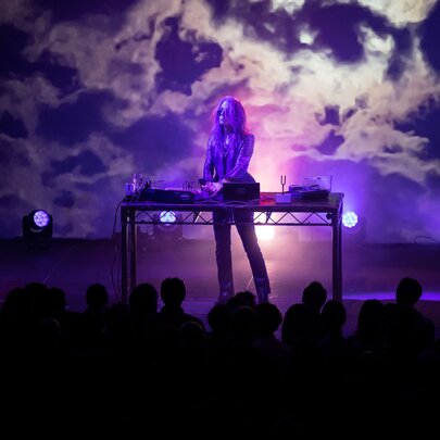 A musician performing on stage with purple-lit cloud like patterns as a backdrop. 