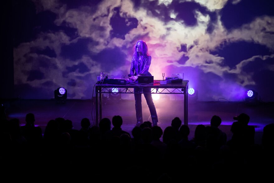 Norwegian musician and composer Bendik Giske performing on stage with purple-lit cloud like patterns as a backdrop. 